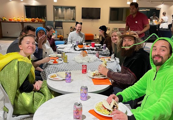 large group of students eat at tables in Borlaug Commons in Halloween costumes