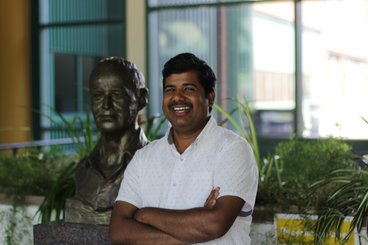 Ashish Ranjan smiling next to a bust of Norman Borlaug on campus